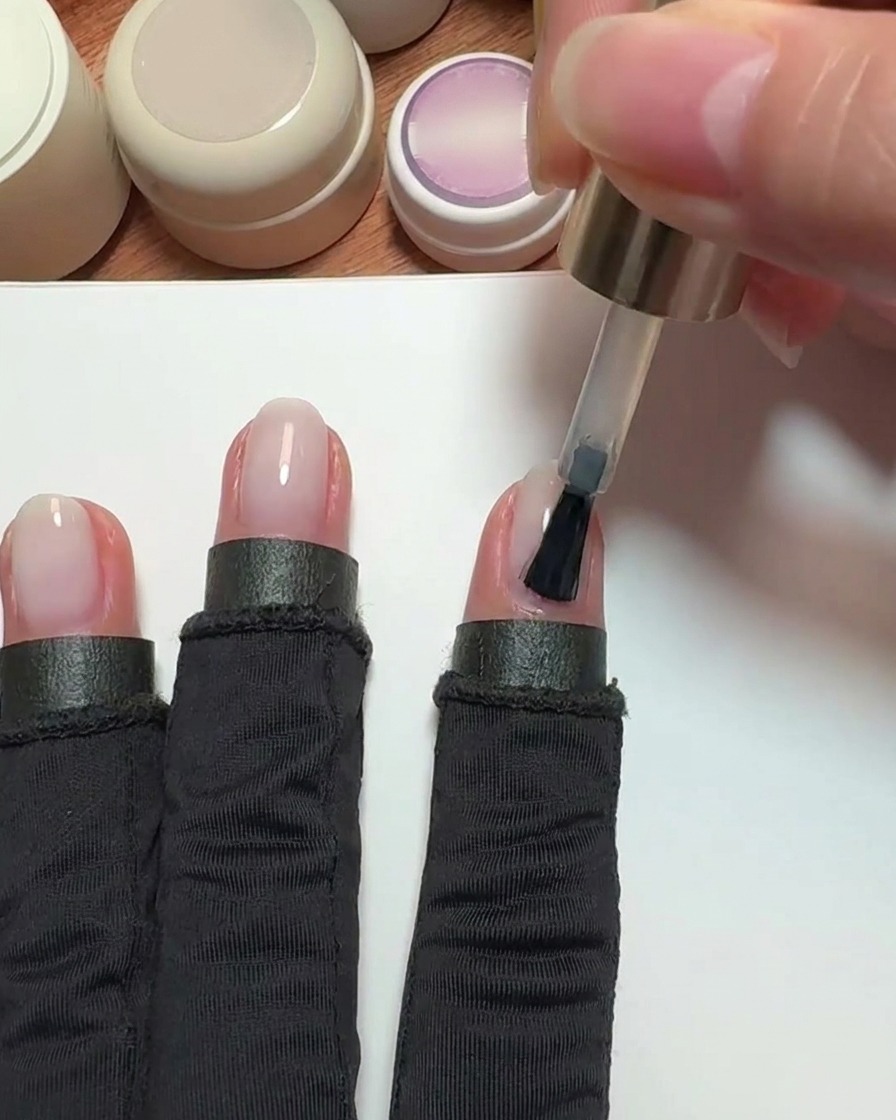 Un pennello che applica smalto gel rosa nude trasparente su ununghia dellindice.