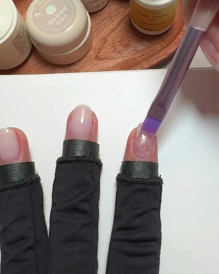 Un pennello che applica smalto cat-eye rosa su ununghia.