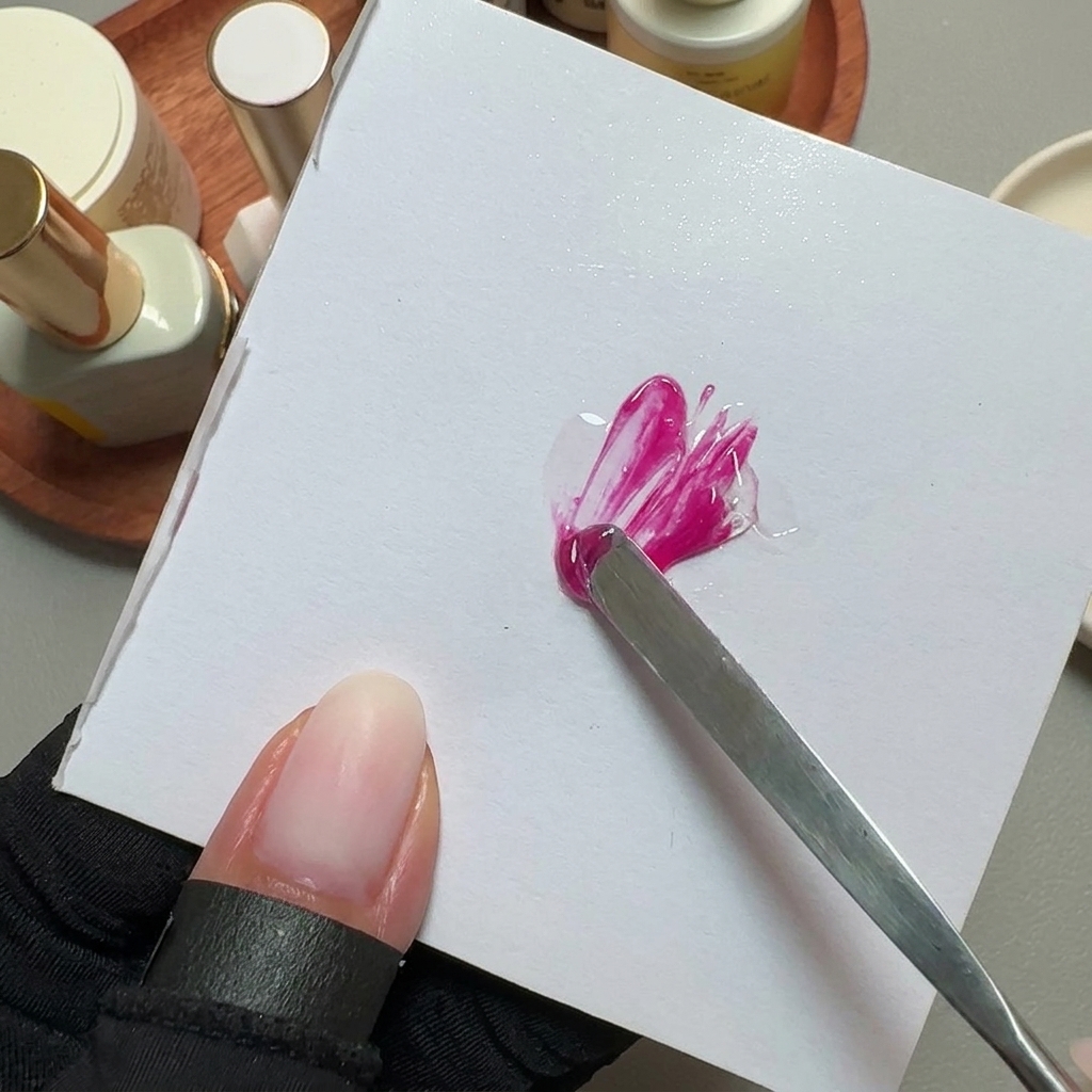 Una spatola di metallo che mescola smalto gel rosa brillante su una tavolozza quadrata bianca.