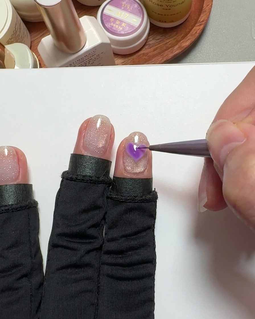 Un pennello a punta fine che riempie una forma a cuore sullunghia con gel rosa.