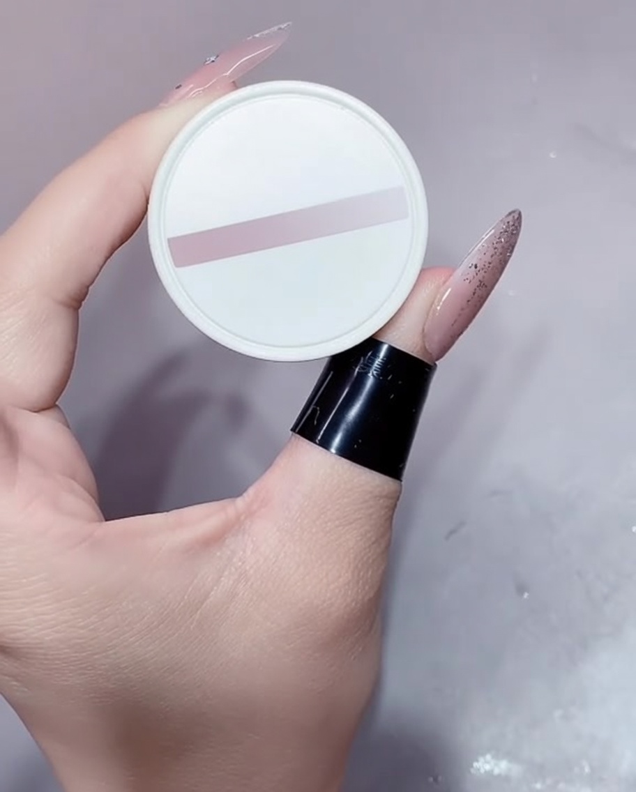 Un piccolo vasetto bianco di smalto gel nude tenuto da una mano con manicure.