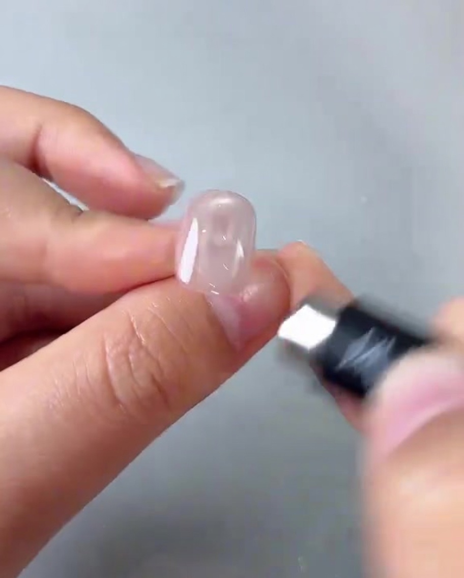 Una mano posiziona un magnete cilindrico sopra ununghia rosa creando un riflesso luminoso.