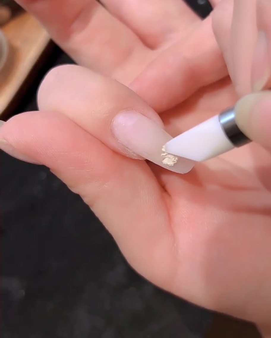 Un pennello per smalto gel che applica uno strato di gel bianco lattiginoso su ununghia naturale.