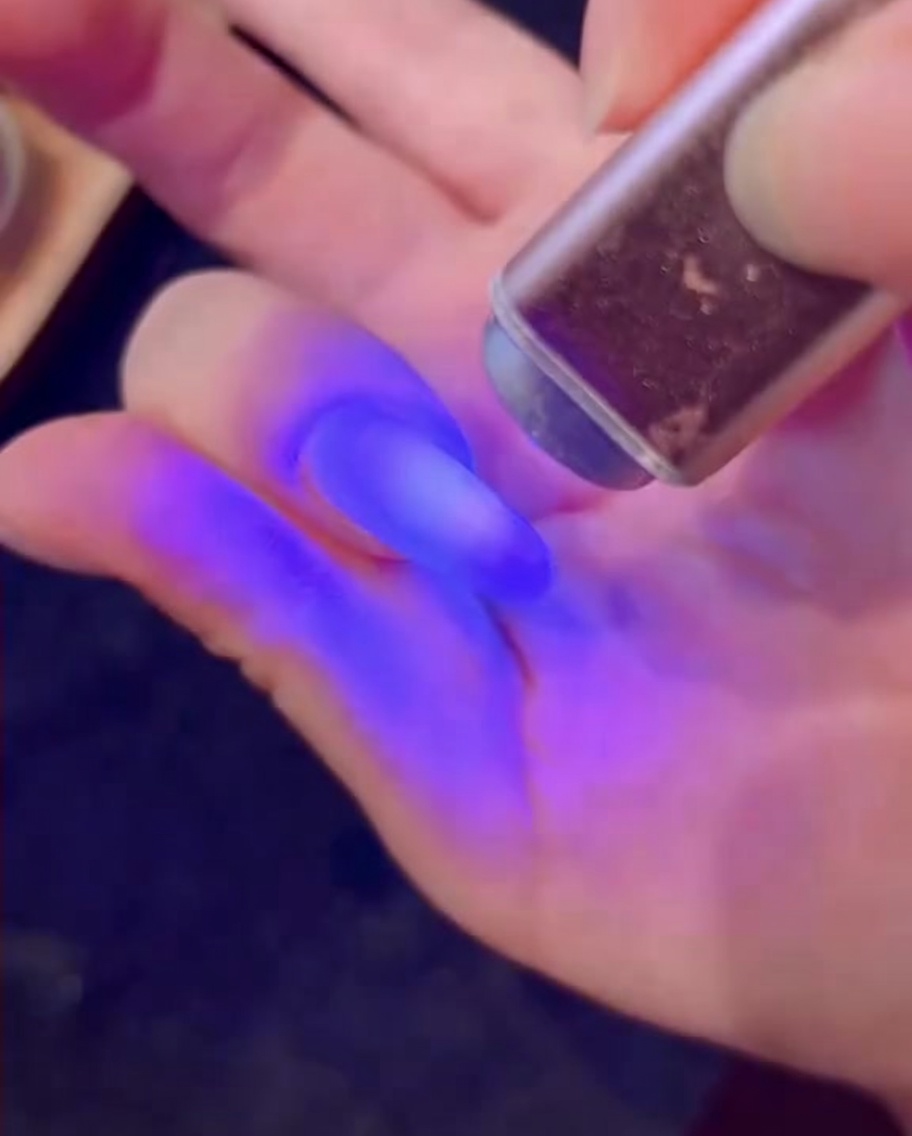 Un pennello che applica uno strato di gel bianco con glitter effetto diamante su ununghia.