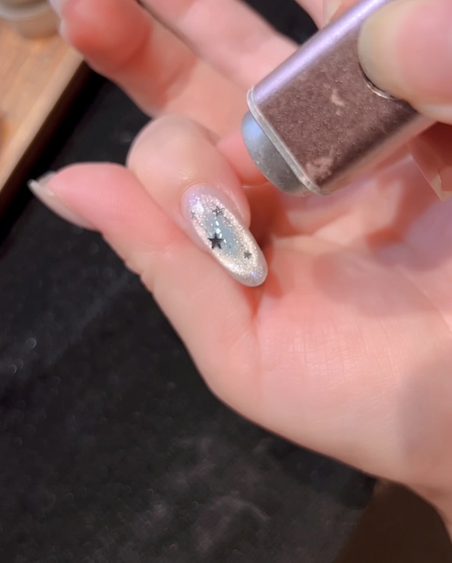 Una lampada UV portatile che polimerizza lunghia decorata con linee argentate e glitter a stella.