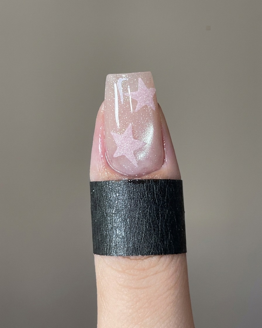 Un pennello fine per nail art che riempie uno stencil a stella su ununghia con gel rosa.