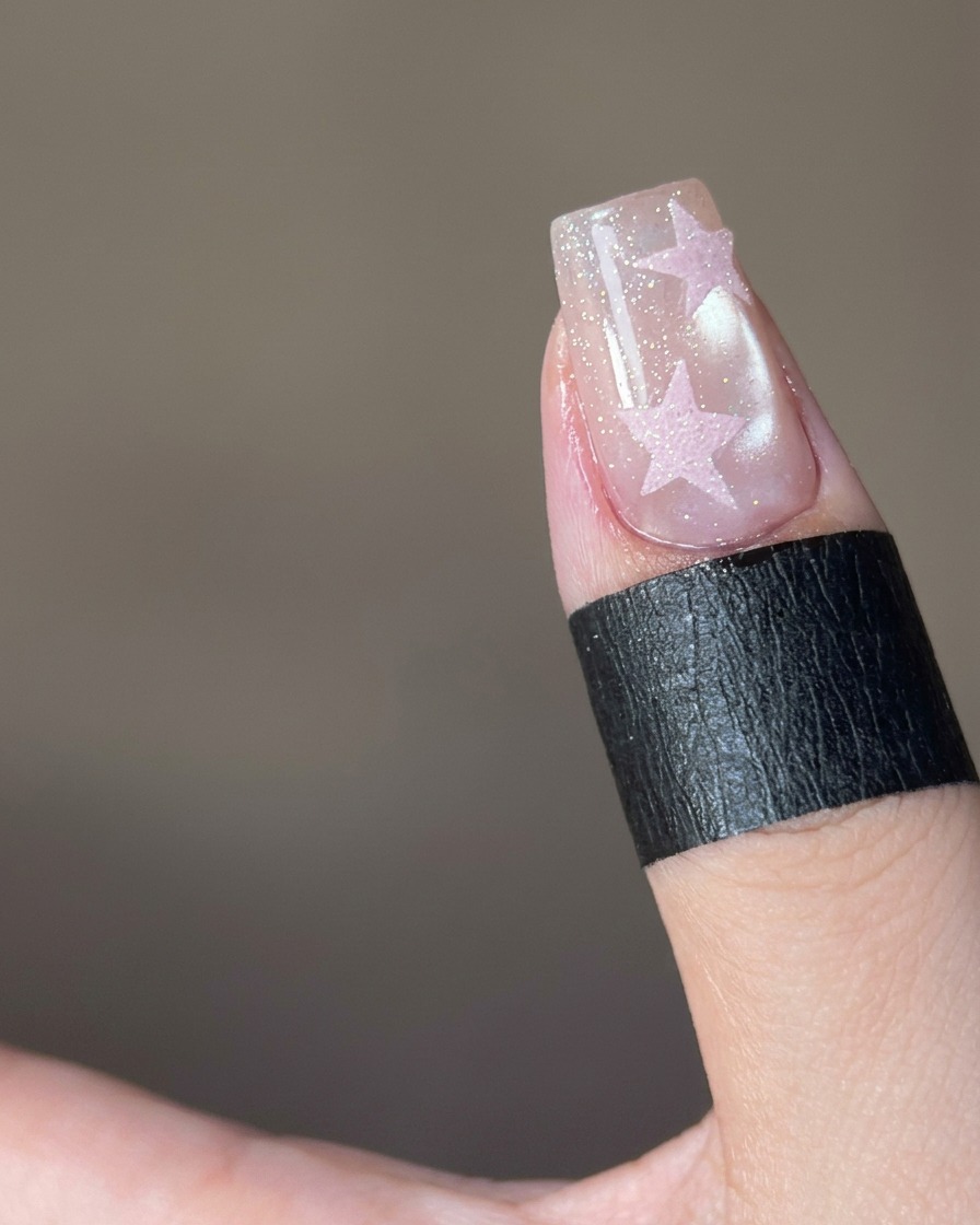Un primo piano che mostra polvere di zucchero rosa cosparsa su un design a forma di stella su ununghia.