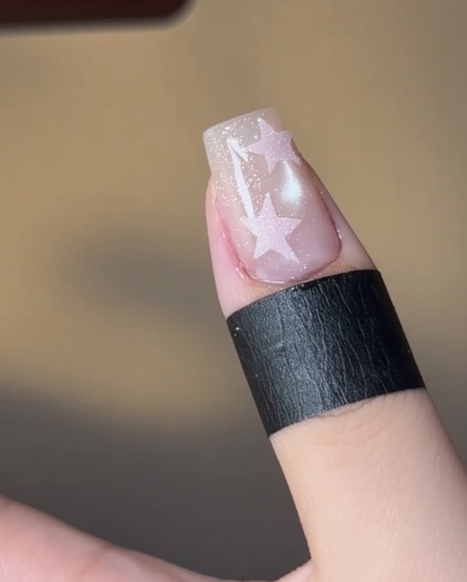Ununghia con un design a stella riempito di rosa che polimerizza sotto una lampada.