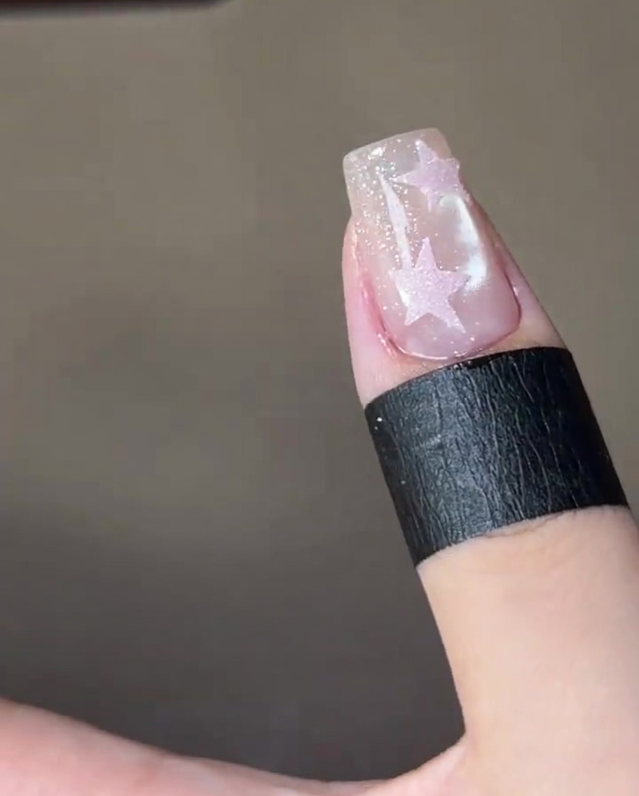 Una vista ravvicinata di un pennello che applica un top coat trasparente lucido sopra una stella rosa dipinta su ununghia scintillante.