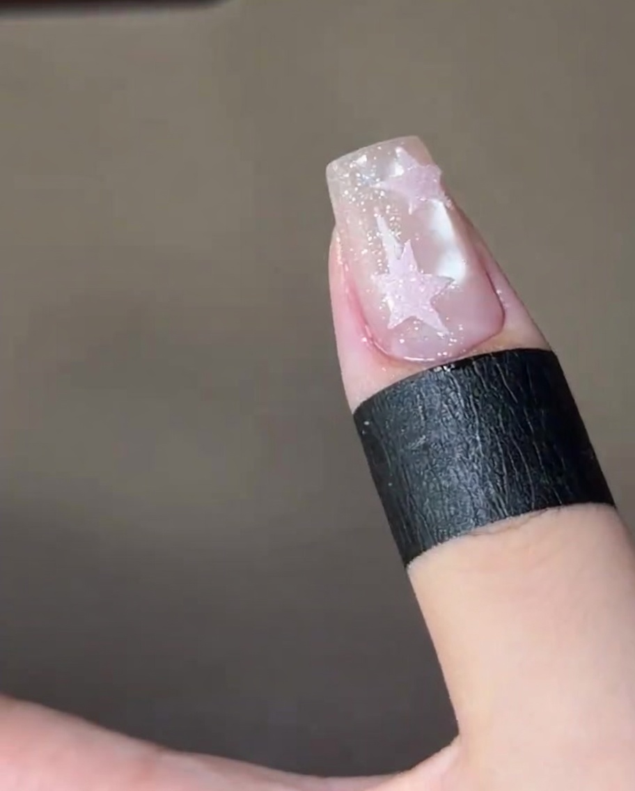 Ununghia finita con due stelle di zucchero rosa testurizzate, che polimerizza allinterno di una lampada UV per unghie.