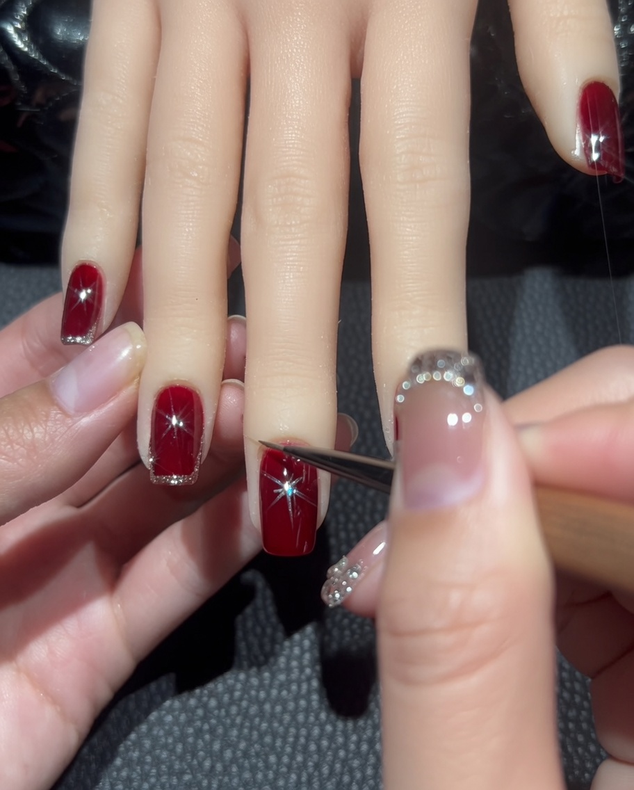 Primo piano di un pennello liner che traccia una sottile linea di glitter oro rosa lungo il bordo di ununghia rossa.