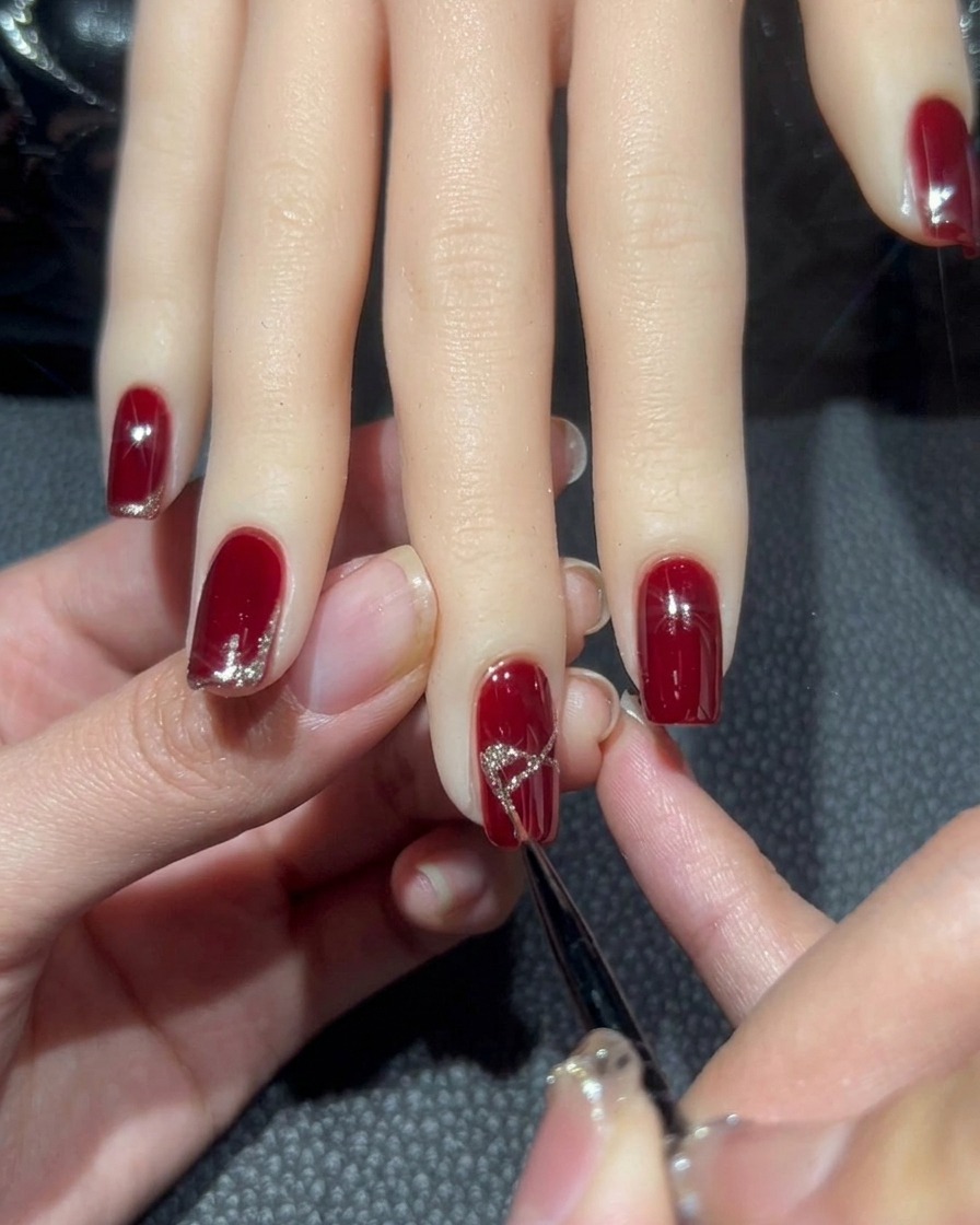 Primo piano dellunghia del dito medio dove la forma a X viene riempita di glitter oro rosa per sembrare un fiocco.