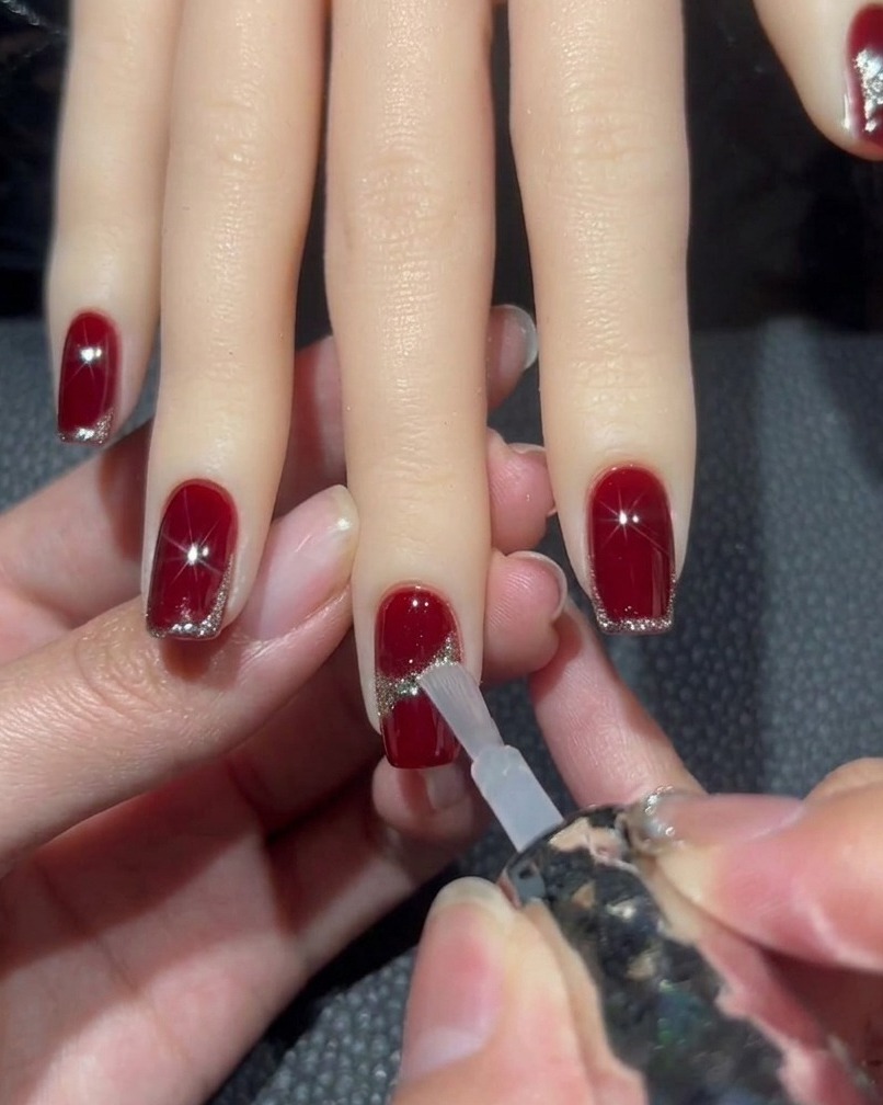 Un pennello che applica un top coat trasparente su ununghia con decorazione, facendo attenzione allo strass centrale.