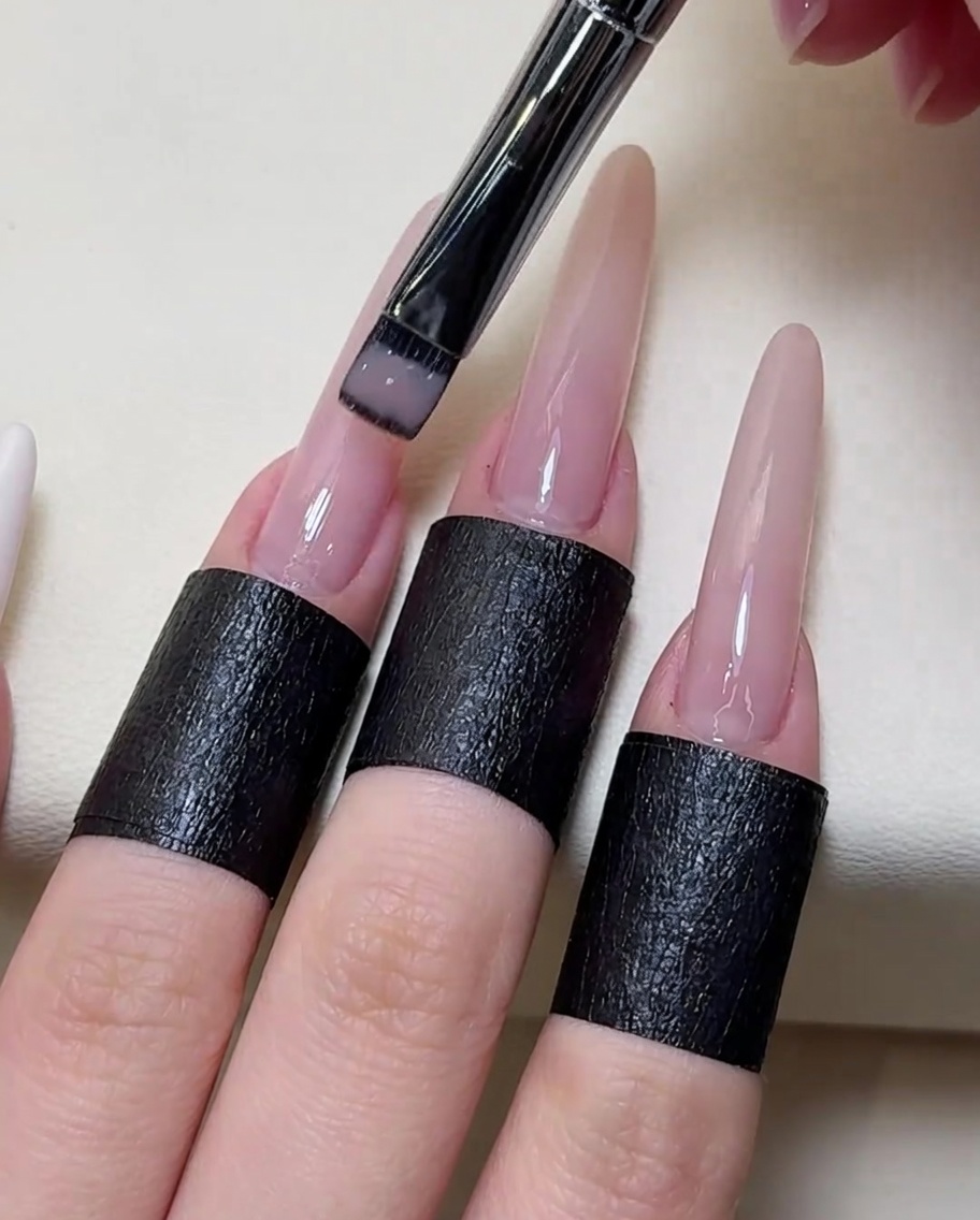Primo piano di un pennello che applica uno smalto gel nude trasparente su tutta la superficie dellunghia.