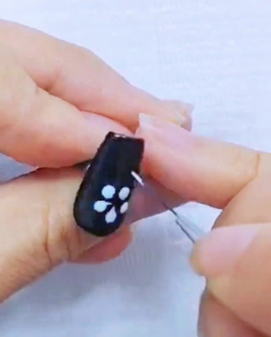 Primo piano di un pennello liner che rifinisce i petali in gel bianco su ununghia nera.