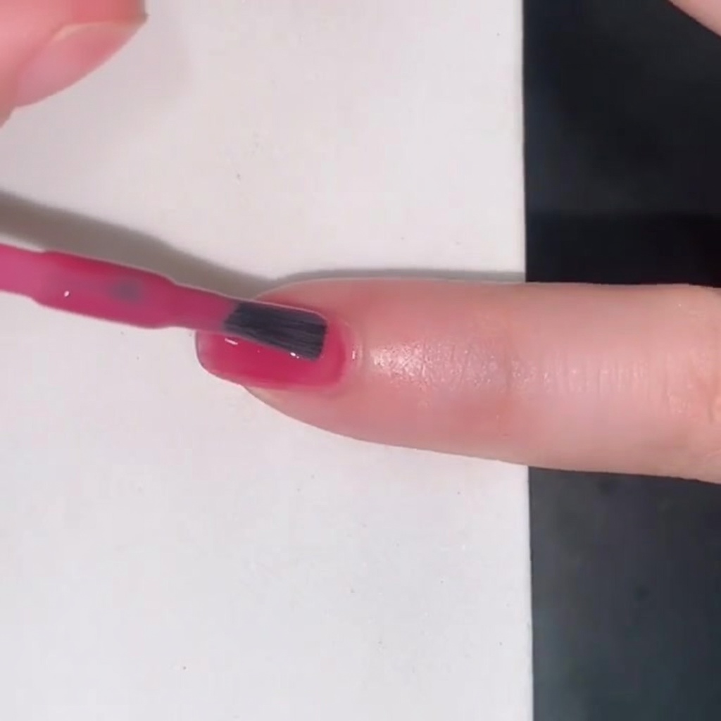 Un pennello che applica uno smalto jelly rosa traslucido su ununghia.