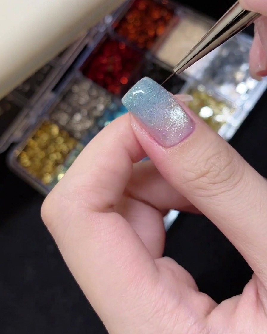 Pinzette che posizionano un piccolo ciondolo glitterato a forma di stella argentata sulla punta di ununghia.
