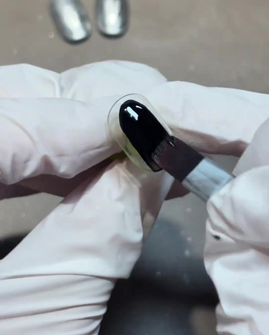 Un pennello che applica uno strato di smalto gel nero coprente sullunghia.