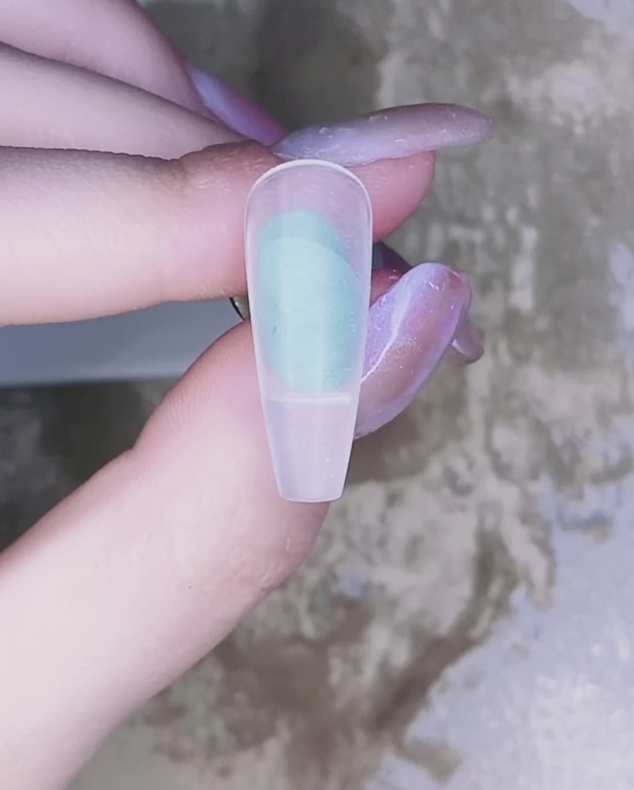 Un primo piano di un pennello che applica uno smalto gel rosa traslucido sulla superficie dellunghia naturale.