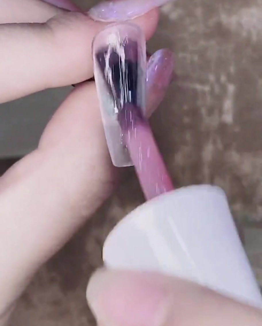 Un pennello che applica un secondo strato di gel rosa traslucido sopra il primo strato polimerizzato.