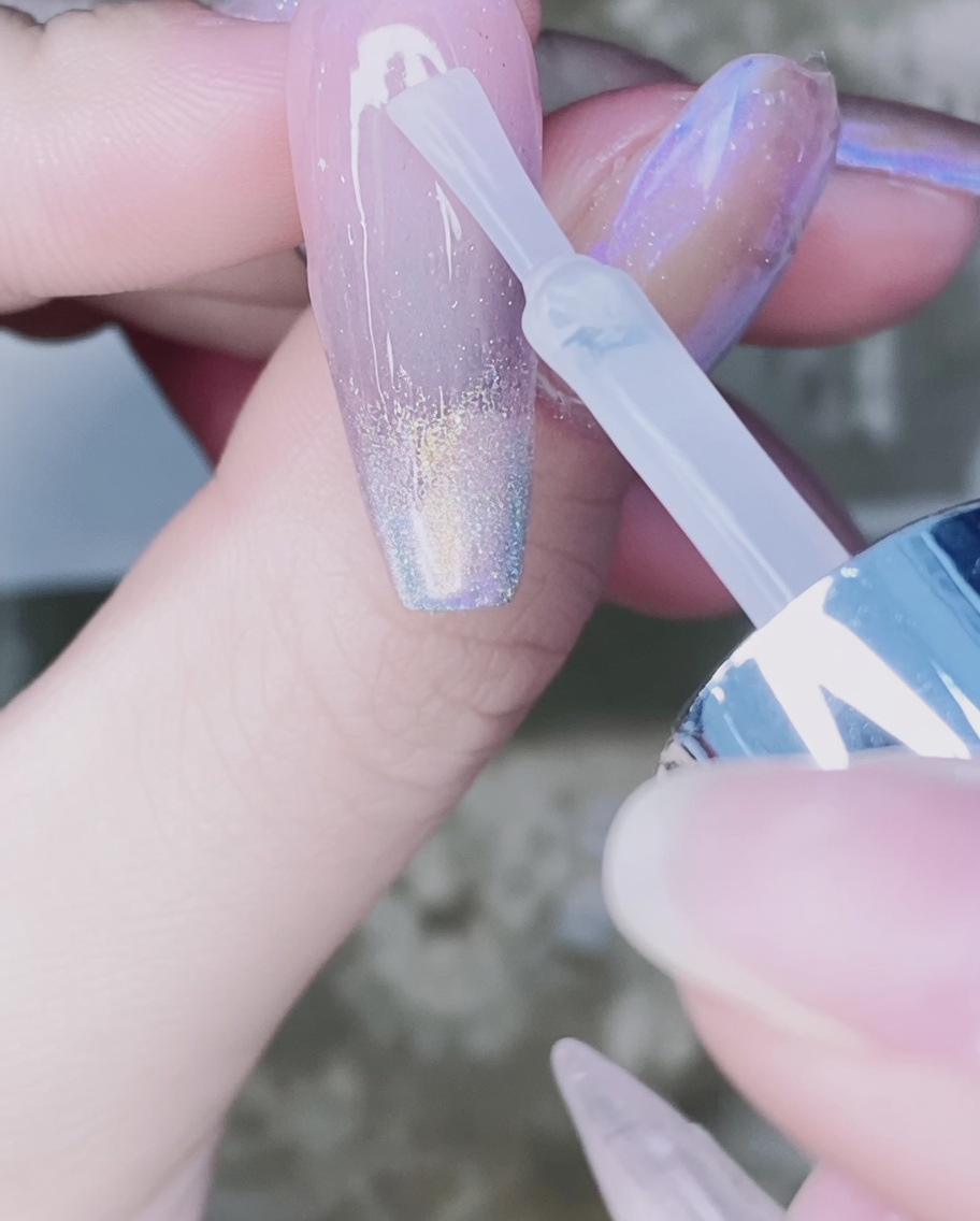Un pennello per unghie che applica il top coat trasparente sopra il gradiente in polvere di cromo sullunghia.