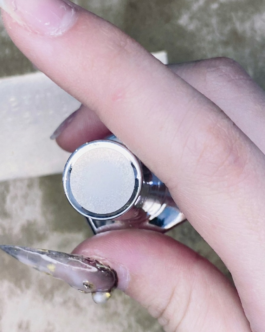 Un pennellino sottile per nail art che applica una piccola goccia di top coat attorno alla base di uno strass montato su ununghia.