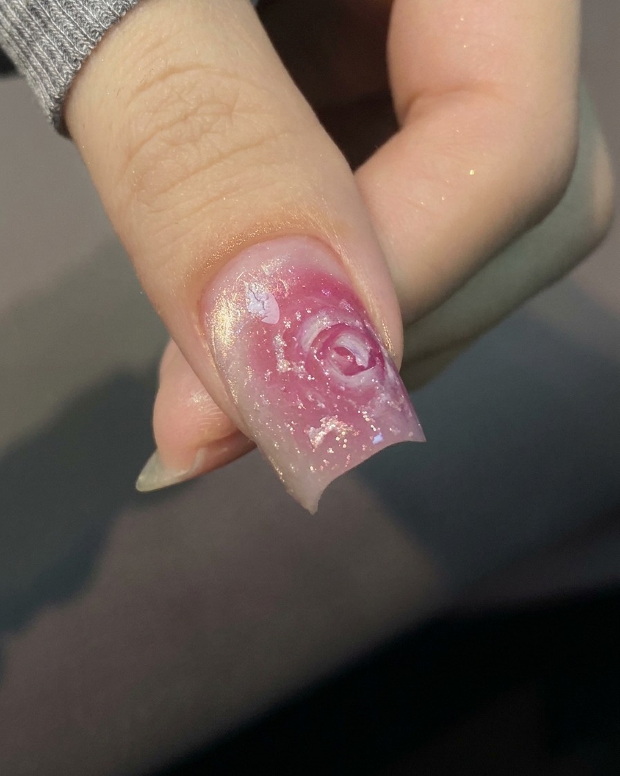 Primo piano di un pennello che applica una base coat trasparente su ununghia naturale.