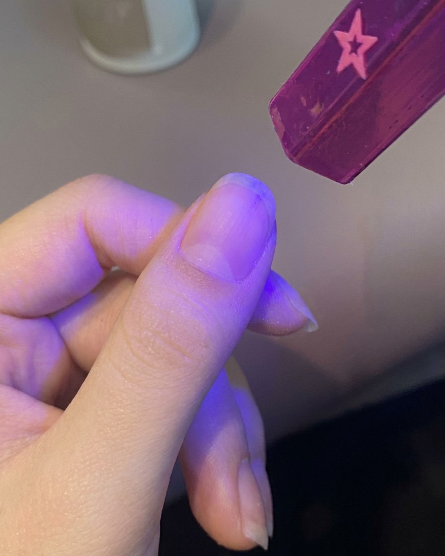 Una mano che inserisce lunghia sotto una piccola lampada UV portatile per polimerizzare la base.