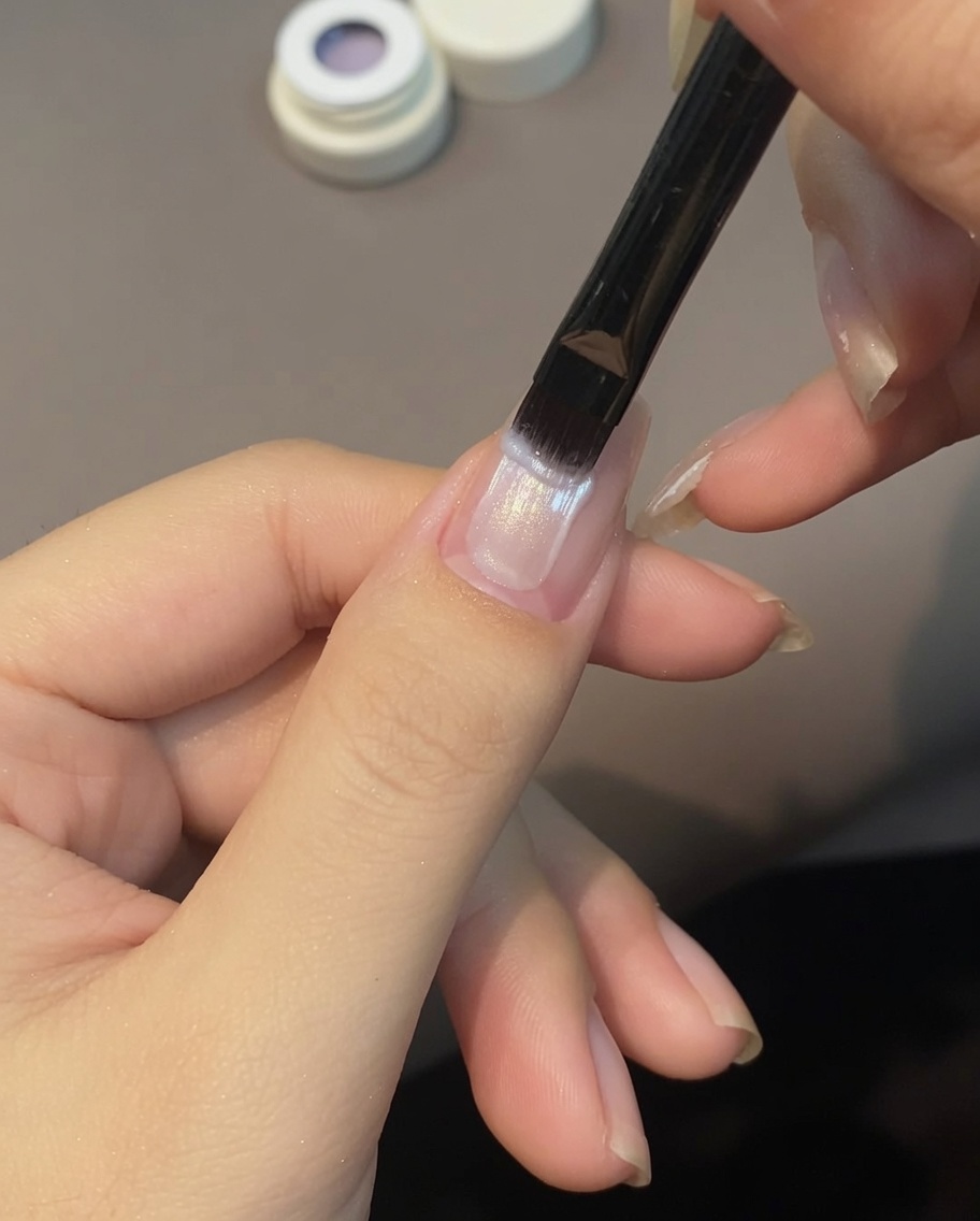 Un pennello che stende il gel cat eye viola chiaro sullunghia.