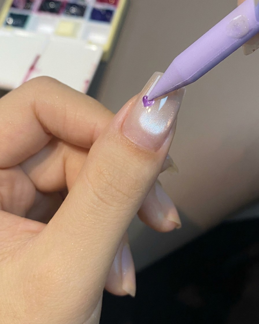 Uno strumento a punta che posiziona una piccola goccia di gel colorato traslucido al centro dellunghia.