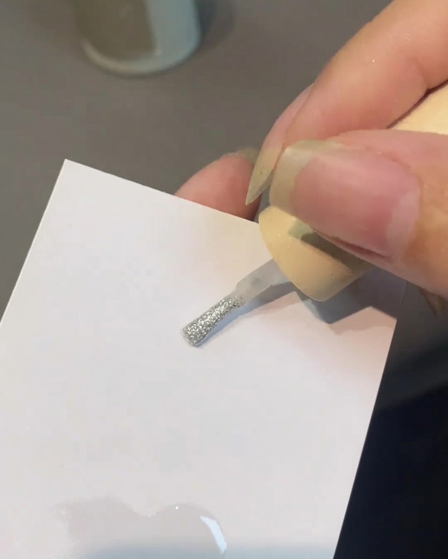 Un pennello che miscela top coat e polvere perlata su una tavolozza.