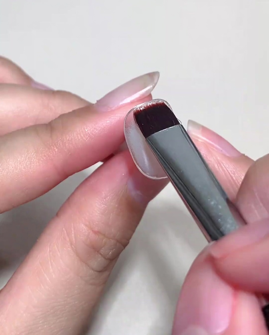 Un pennello applica uno strato di gel cat-eye nude sopra ununghia già trattata con base coat.