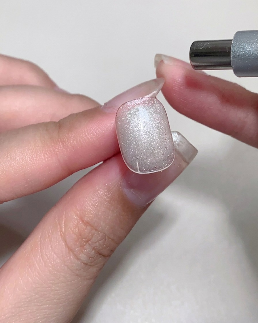 Un magnete viene utilizzato sopra ununghia con gel cat-eye ancora umido per creare un riflesso brillante.