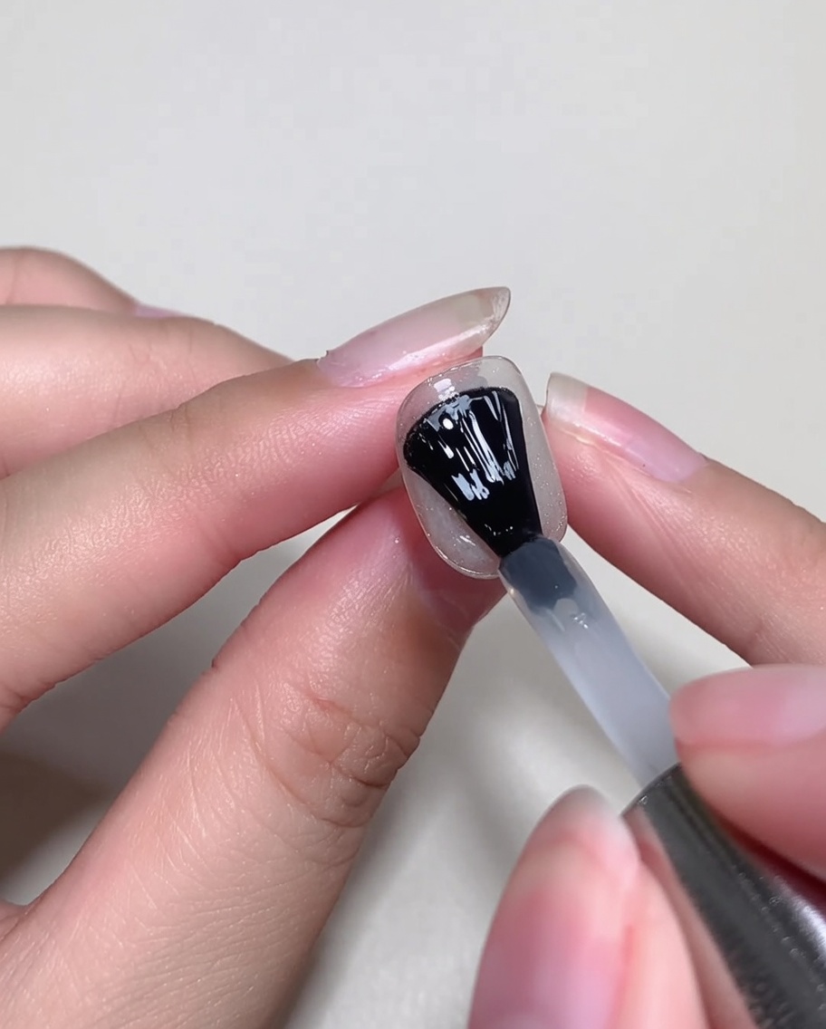 Un pennello applica un sottile strato di blooming gel trasparente sopra lunghia decorata.
