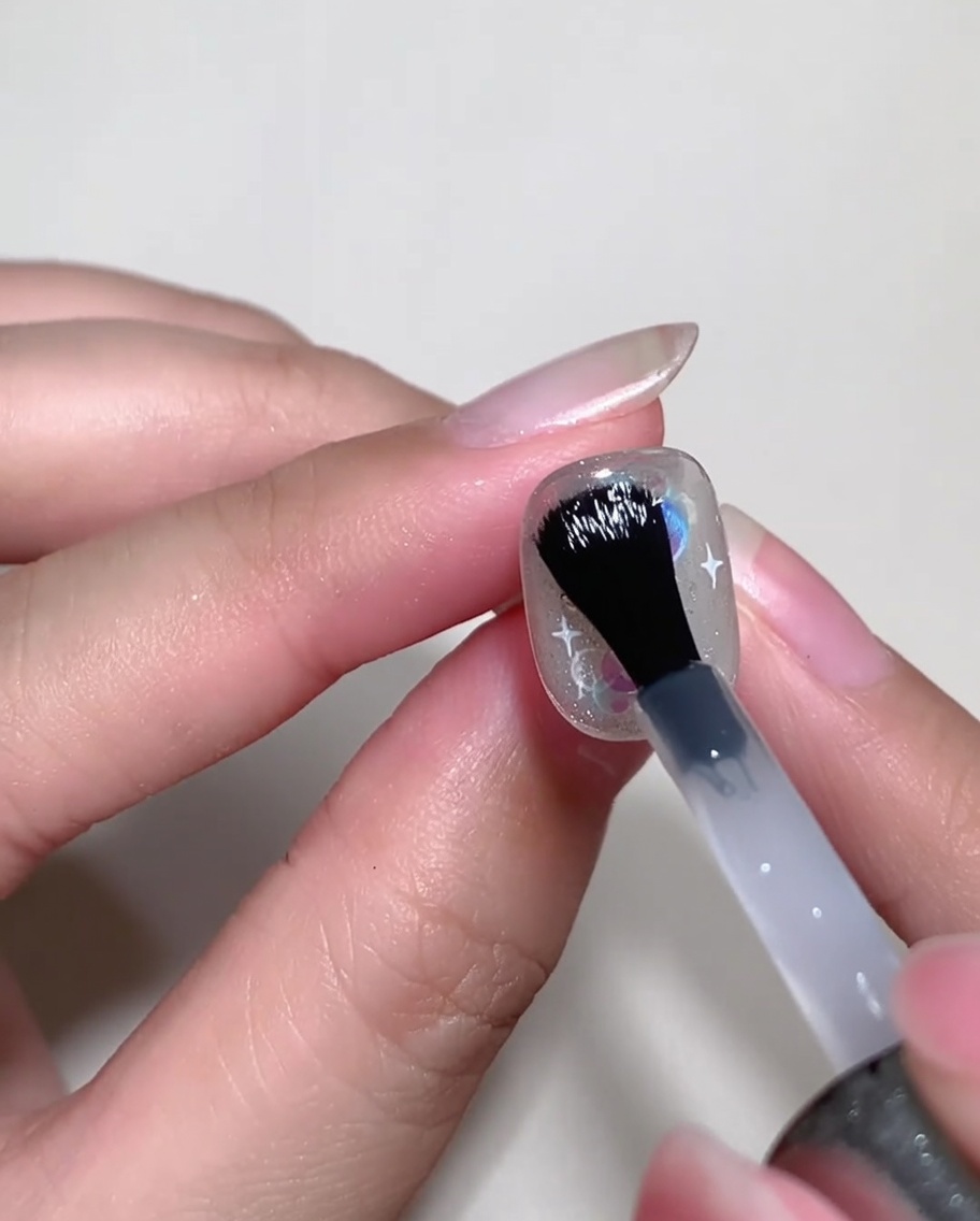 Un pennello applica del builder gel trasparente sullunghia decorata per livellarne la superficie.