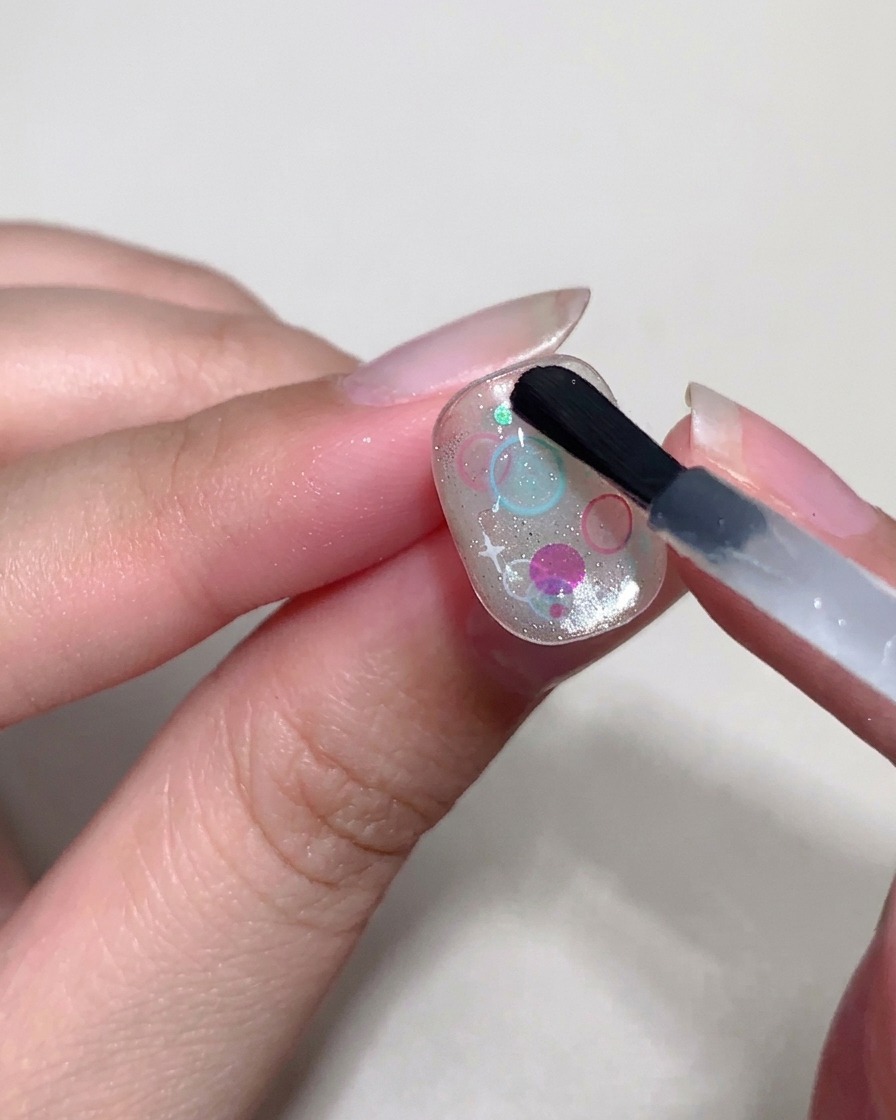 Un pennello di precisione utilizza un top coat denso per formare piccole bolle in rilievo sopra le paillettes.