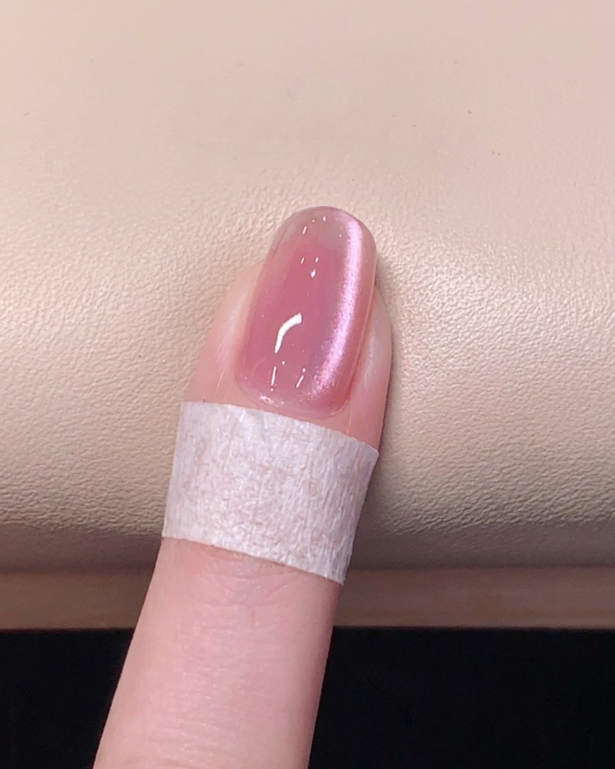 Un pennello applica un top coat trasparente e lucido su ununghia in gel cat eye magnetico rosa.