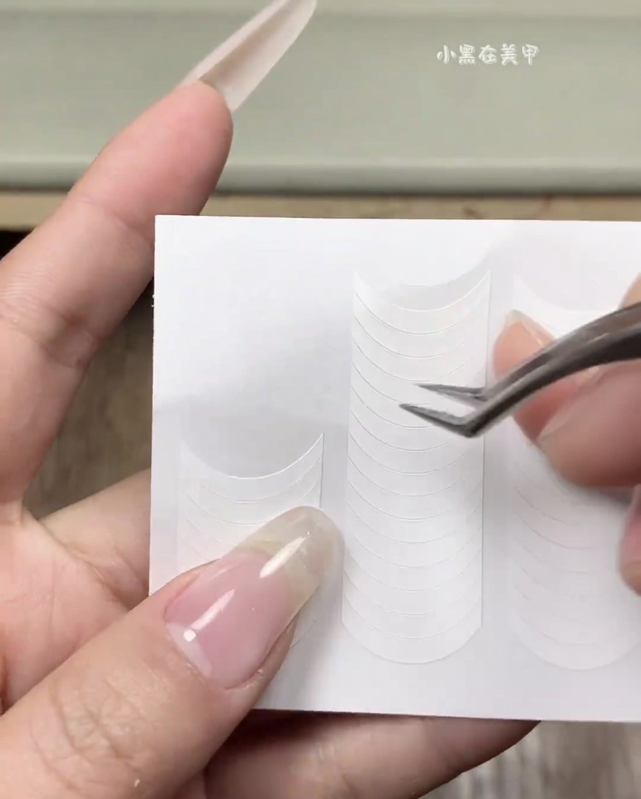 Una mano che applica una linea guida adesiva bianca per french su ununghia naturale pulita.