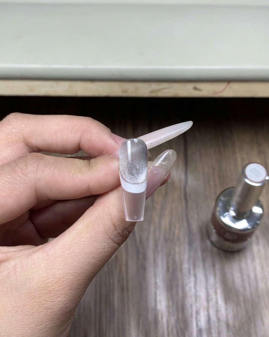 Primo piano di una piccola boccetta di vetro di top coat gel specifico per polvere cromata appoggiata su una superficie di legno.