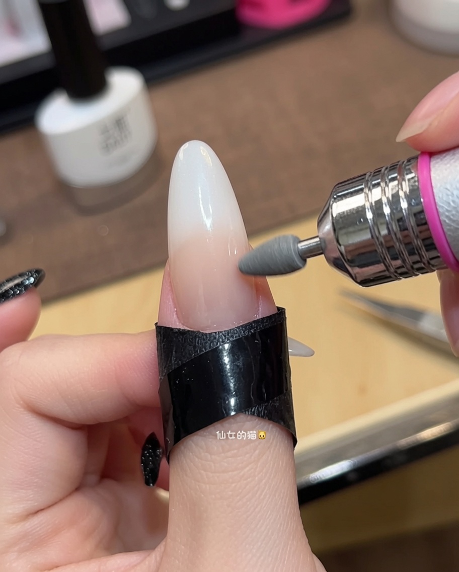 Primo piano di un pennello che applica una seconda passata di smalto gel nude traslucido su ununghia.