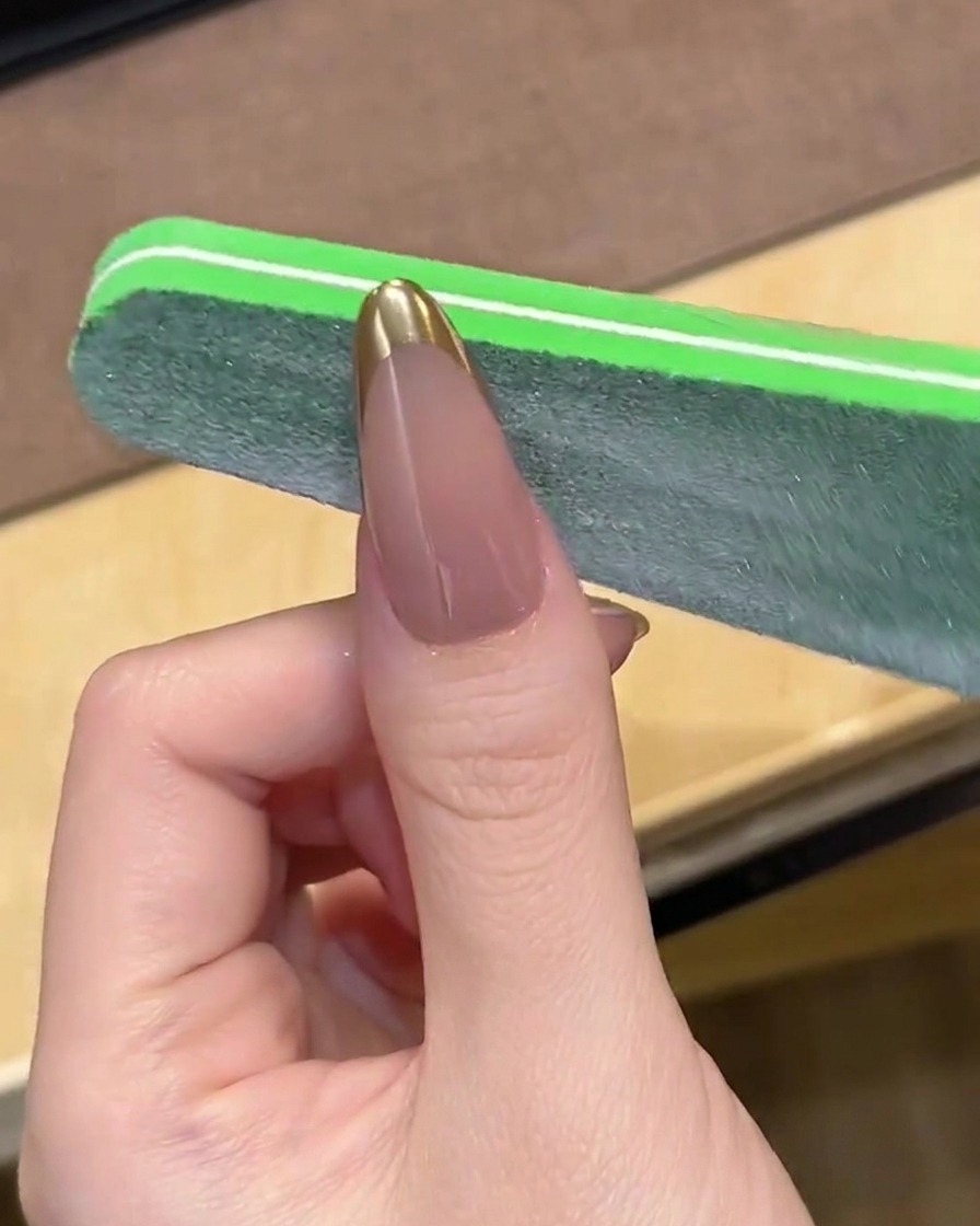 Una lima per unghie che leviga delicatamente la punta di una French manicure cromata.