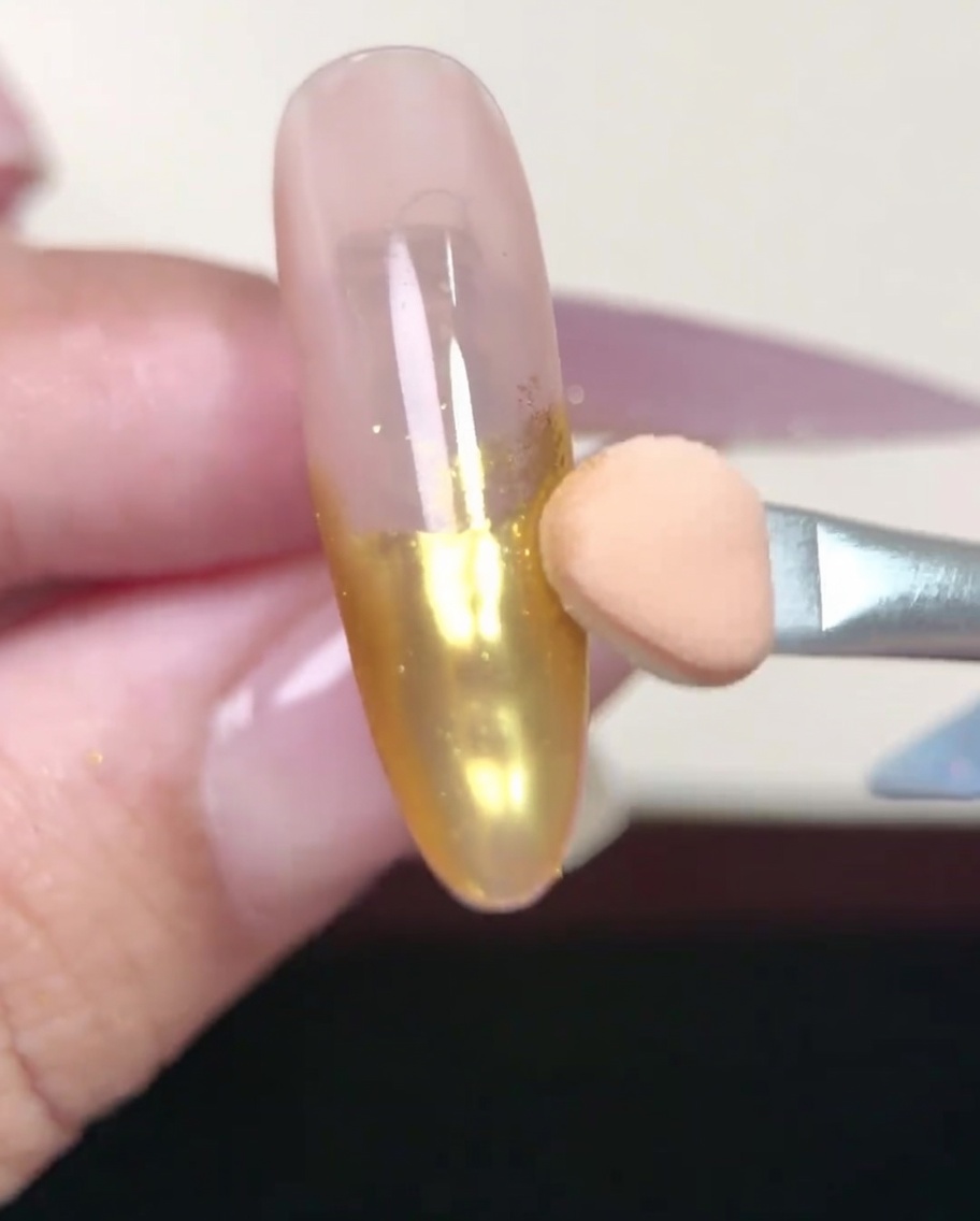 Pennello per unghie che stende uno strato di base gel nude su ununghia a mandorla.