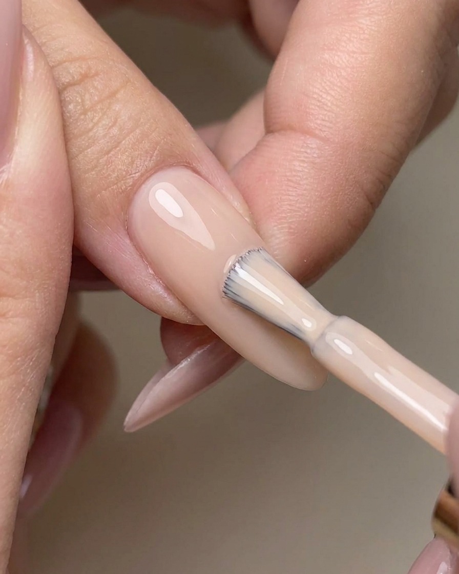 Pennello che stende un top coat trasparente senza dispersione su ununghia con base nude.