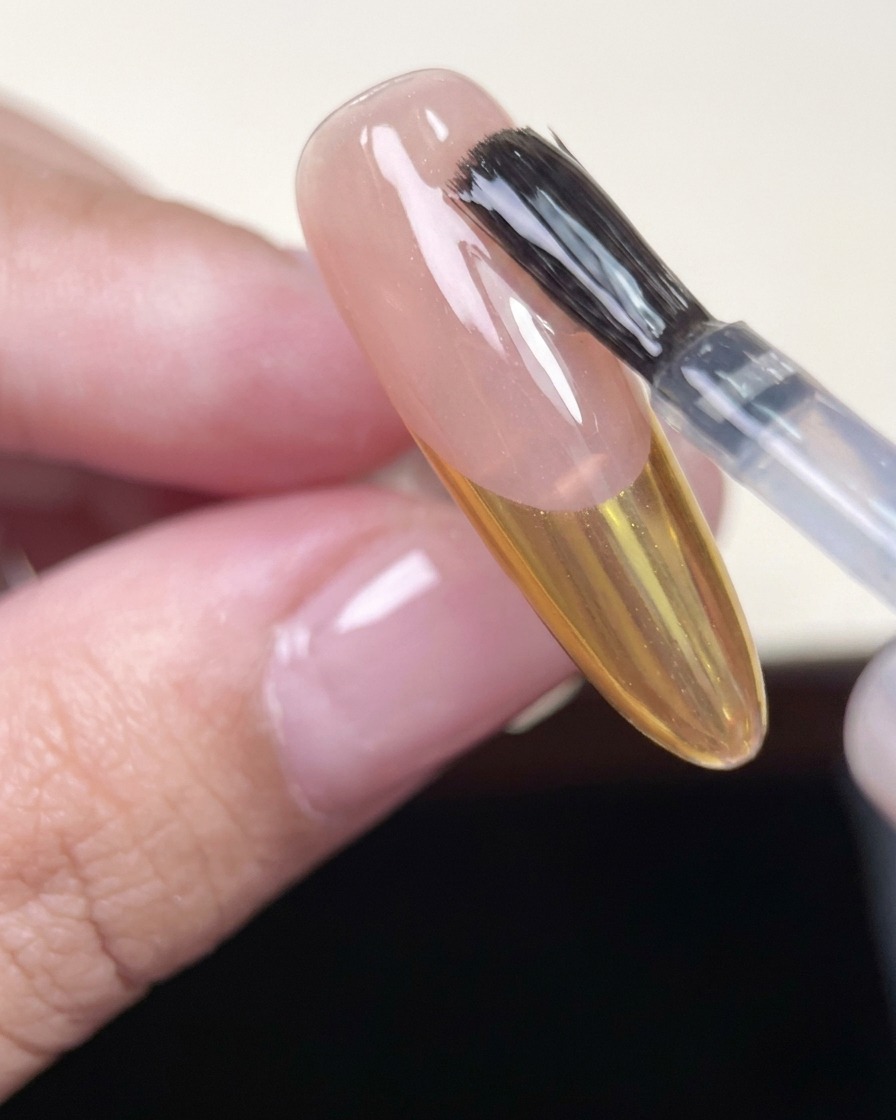 Pennello che stende un top coat lucido su ununghia a mandorla con French cromo oro.