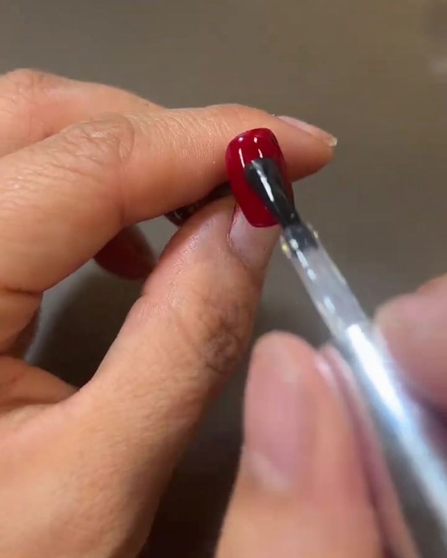 Pennello che stende uno strato fresco e lucido di top coat trasparente sopra il gel rosso, creando una superficie riflettente.