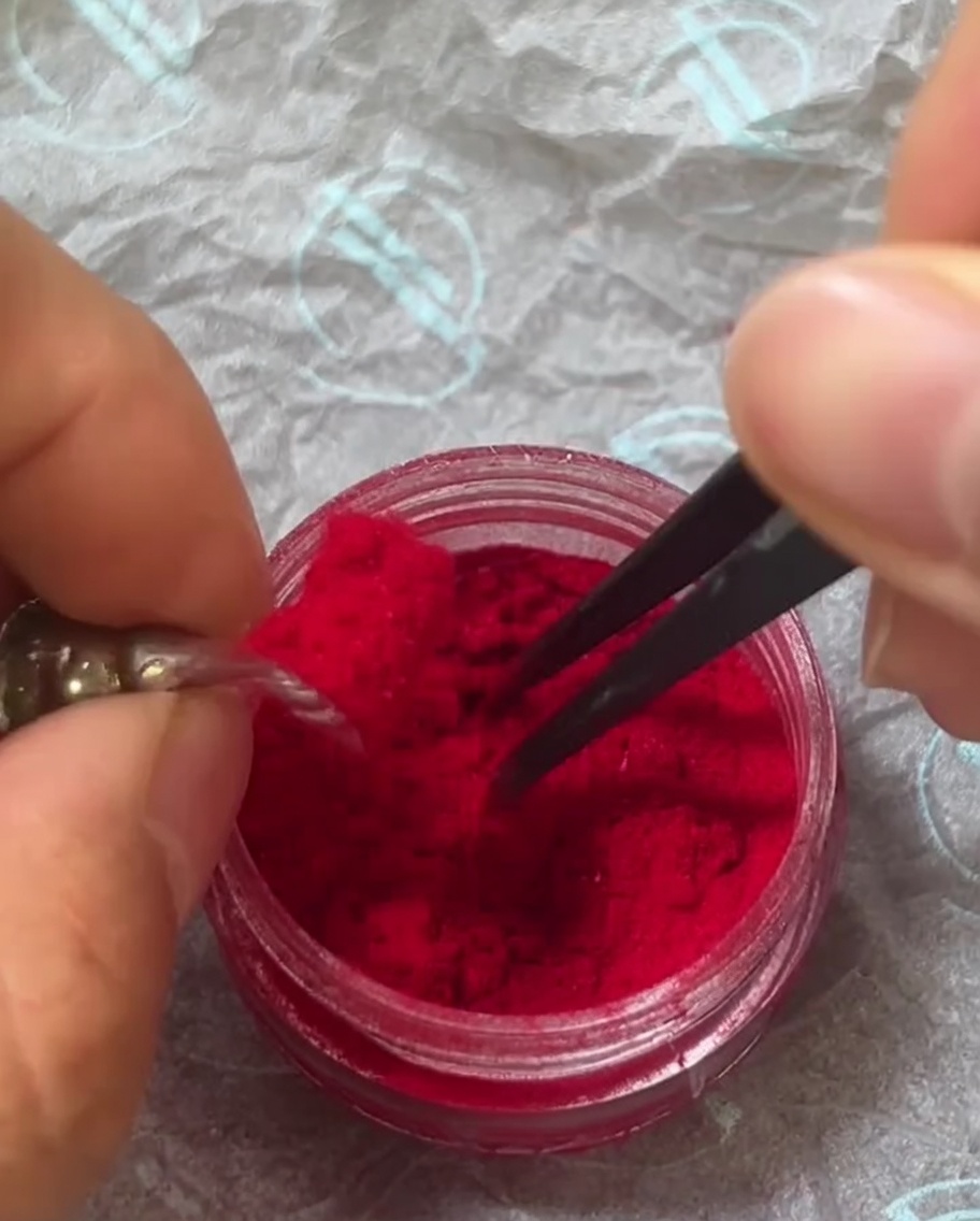 Pinzette che cospargono delicatamente la polvere rossa sullunghia rivestita di gel umido.