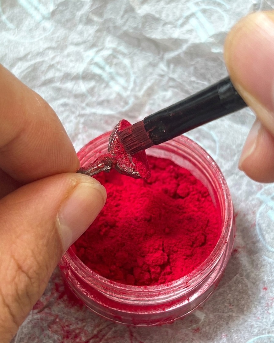Un dito che preme leggermente sulla polvere vellutata per fissarla nel gel umido.
