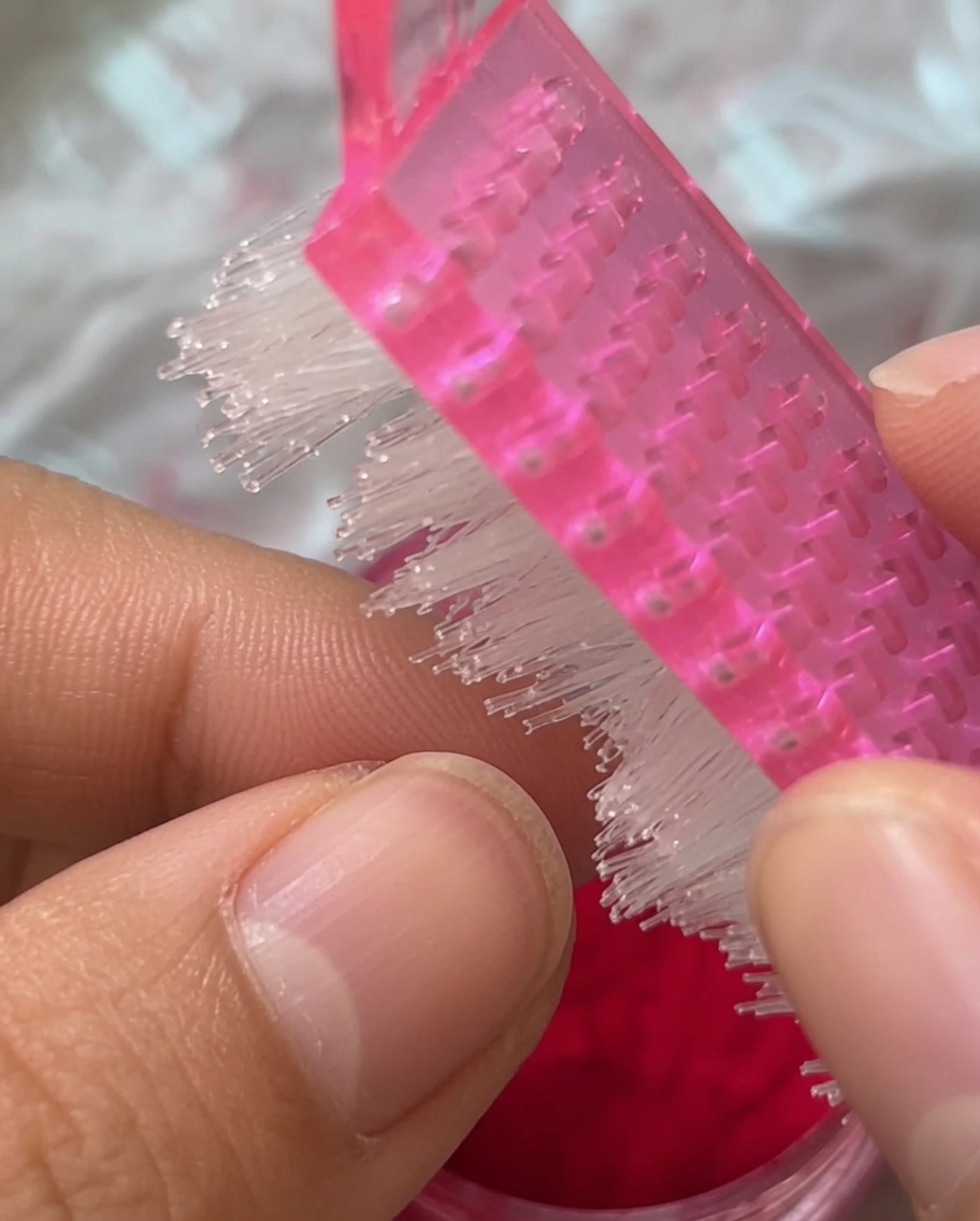 Primo piano di un pennello da manicure rosa che spazza sopra ununghia rivestita di polvere vellutata.