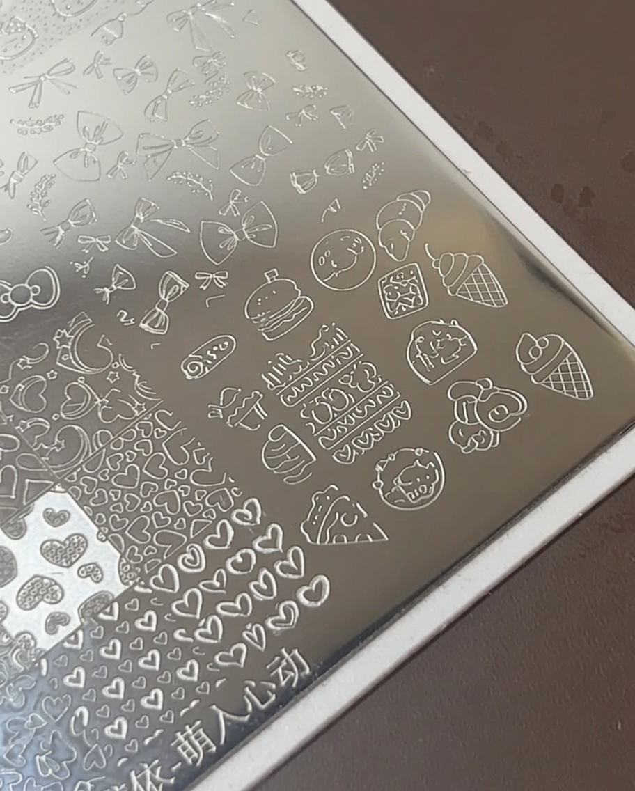 Pennello da nail art che applica smalto bianco denso sopra icone di cibo incise su una piastra per stamping metallica.
