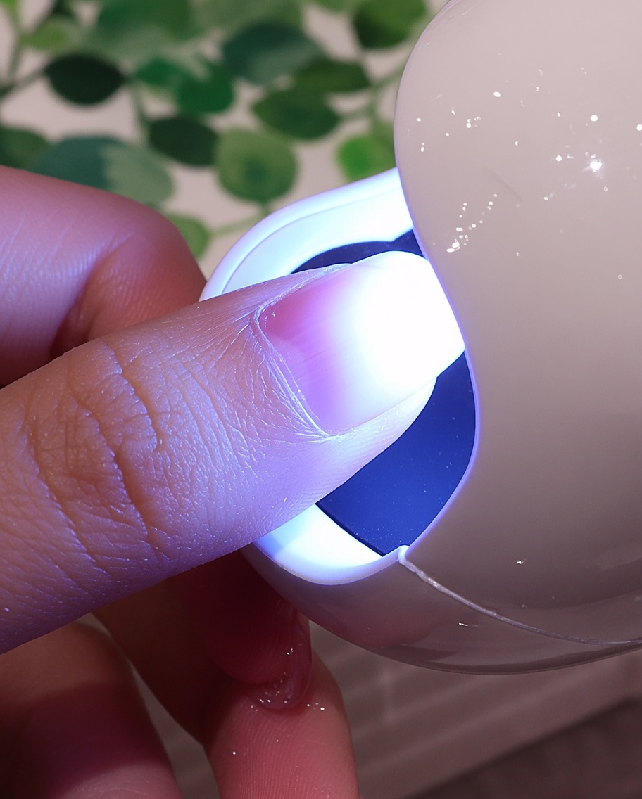 Ununghia con un rivestimento bianco materico posizionata sotto la luce viola di una piccola lampada UV/LED.